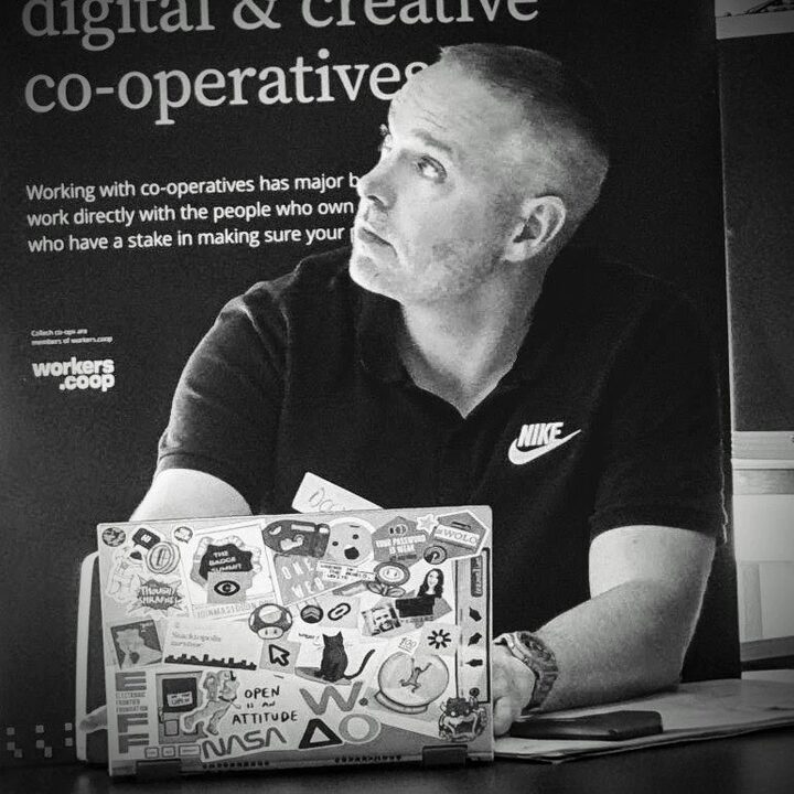 Doug at a co-operatives event, glancing sideways over a laptop covered in stickers
